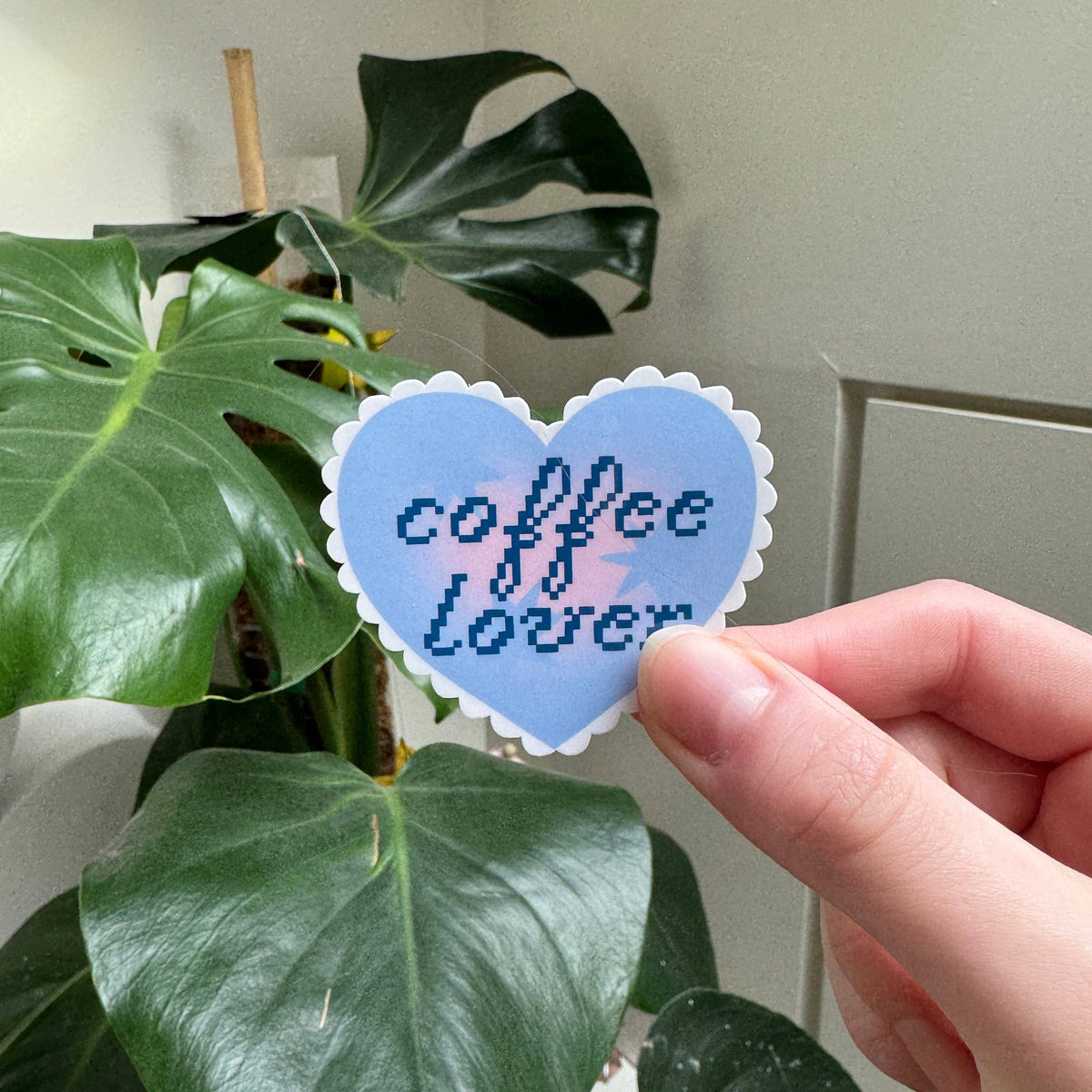 Heart-shaped sticker in light blue with dark pixel text held in hand