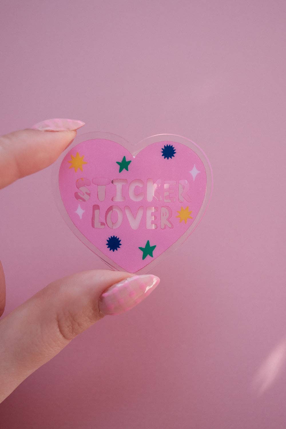 Heart-shaped notebook clip held in fingers, pink “Sticker Lover” with star icons