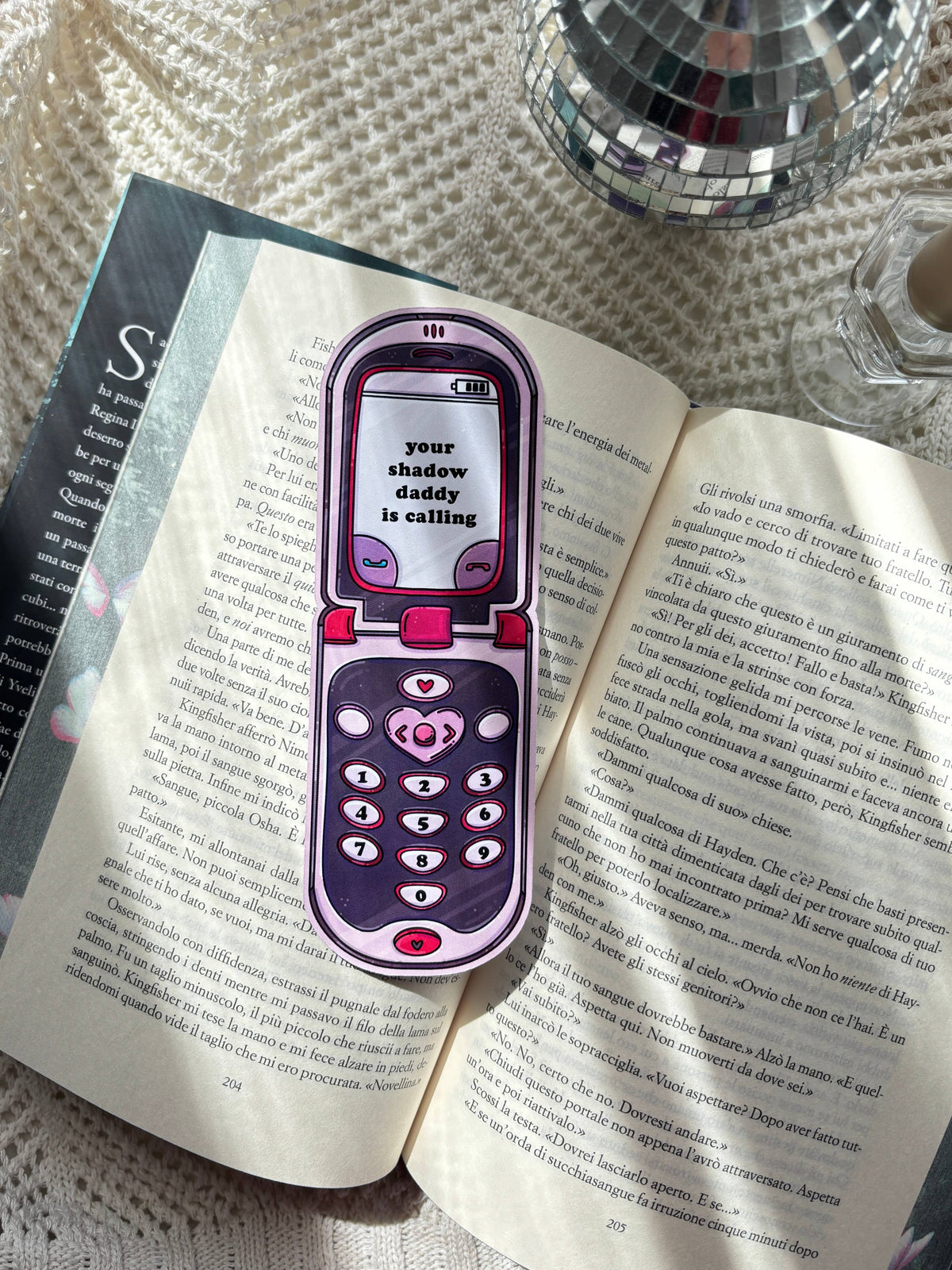 Purple and pink phone-shaped bookmark clipped to open book pages.