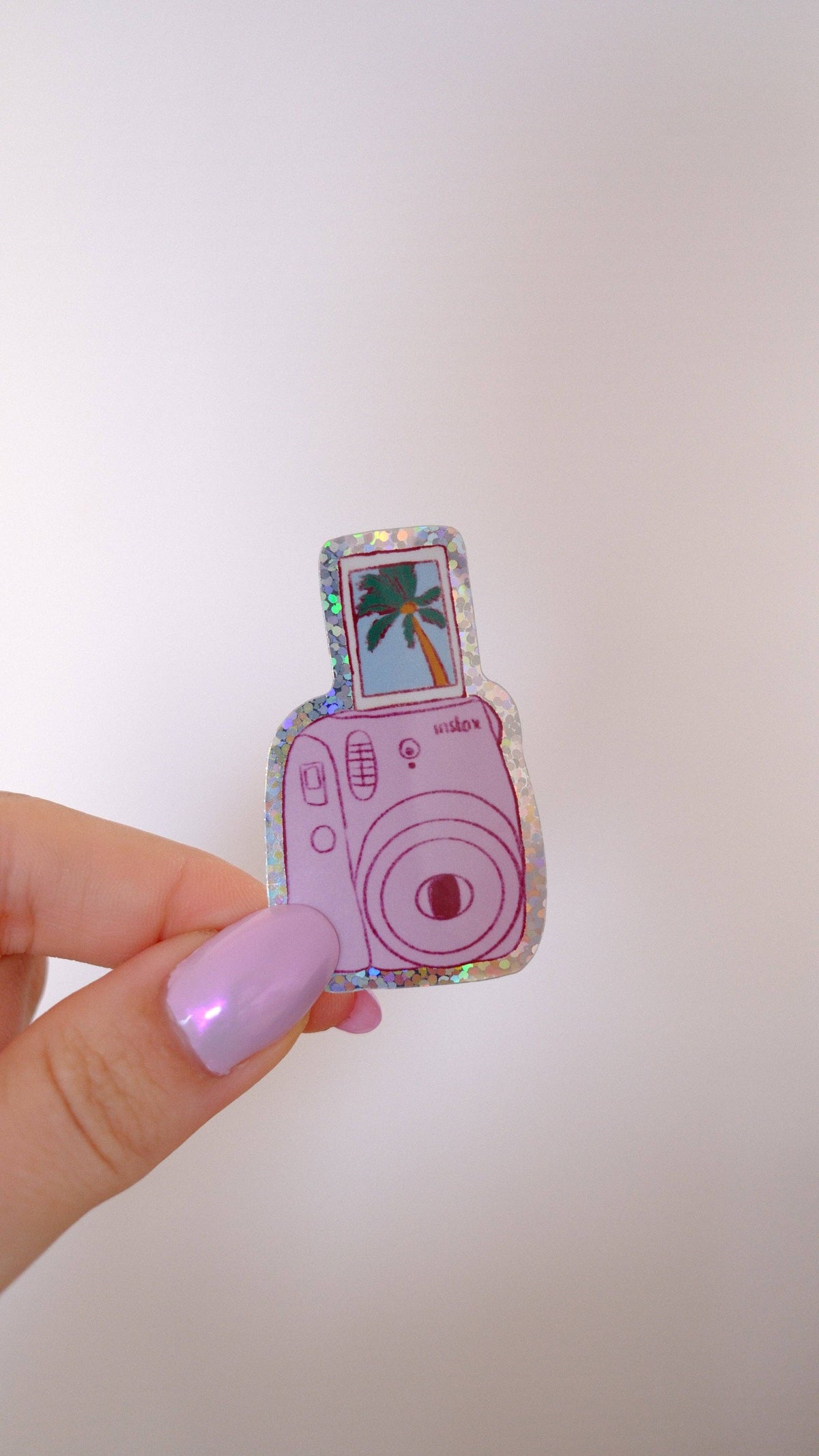 Pink polaroid camera sticker with palm tree photo, held between fingers