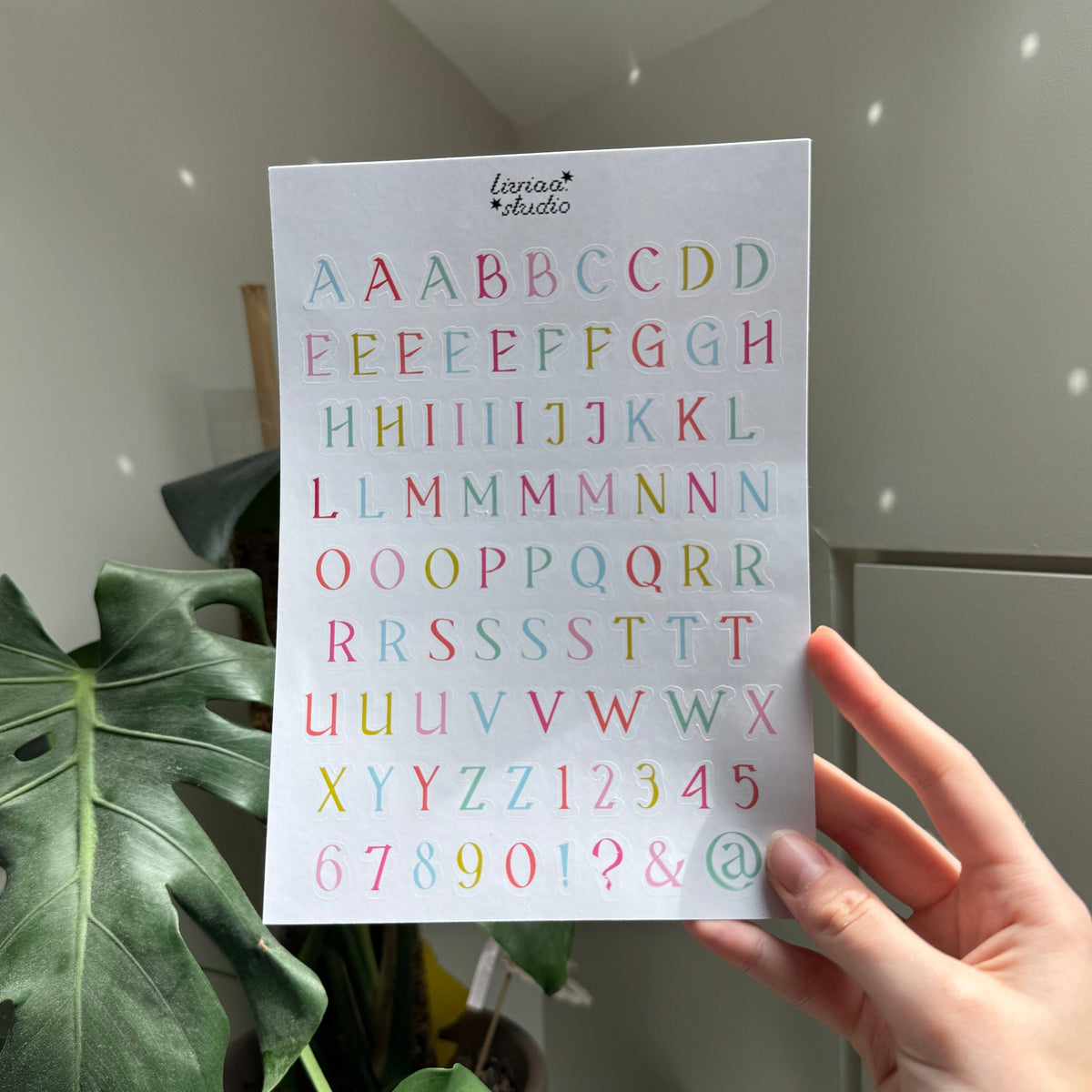 Multicolor letter sticker sheet held by hand, showing letters and symbols