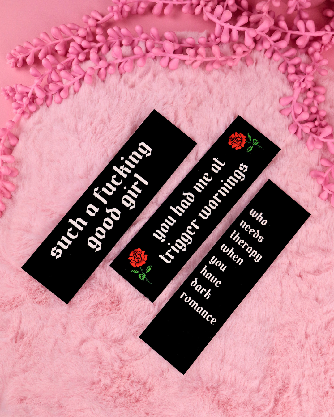 Set of three black bookmarks with red roses and green text on pink fuzzy surface