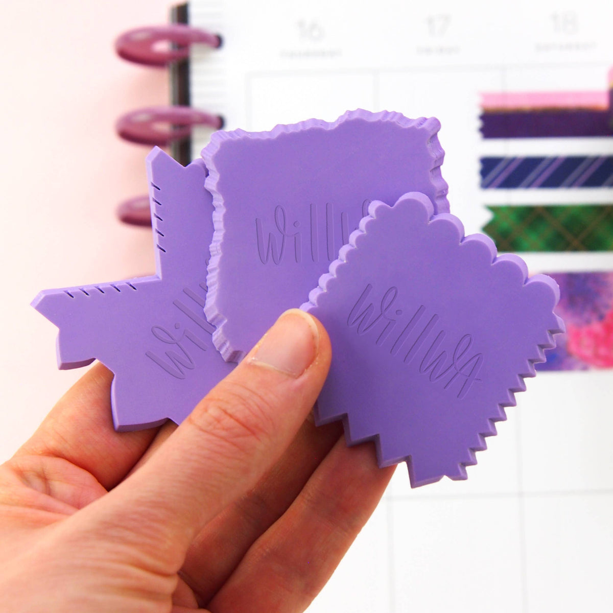 Purple house-shaped washi cutter held in a hand, with serrated side edges