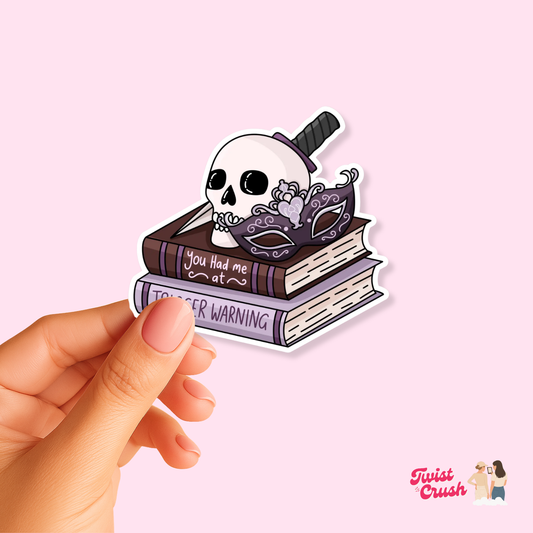 Book-themed sticker: cute skeleton reading on stacked books, held by a hand