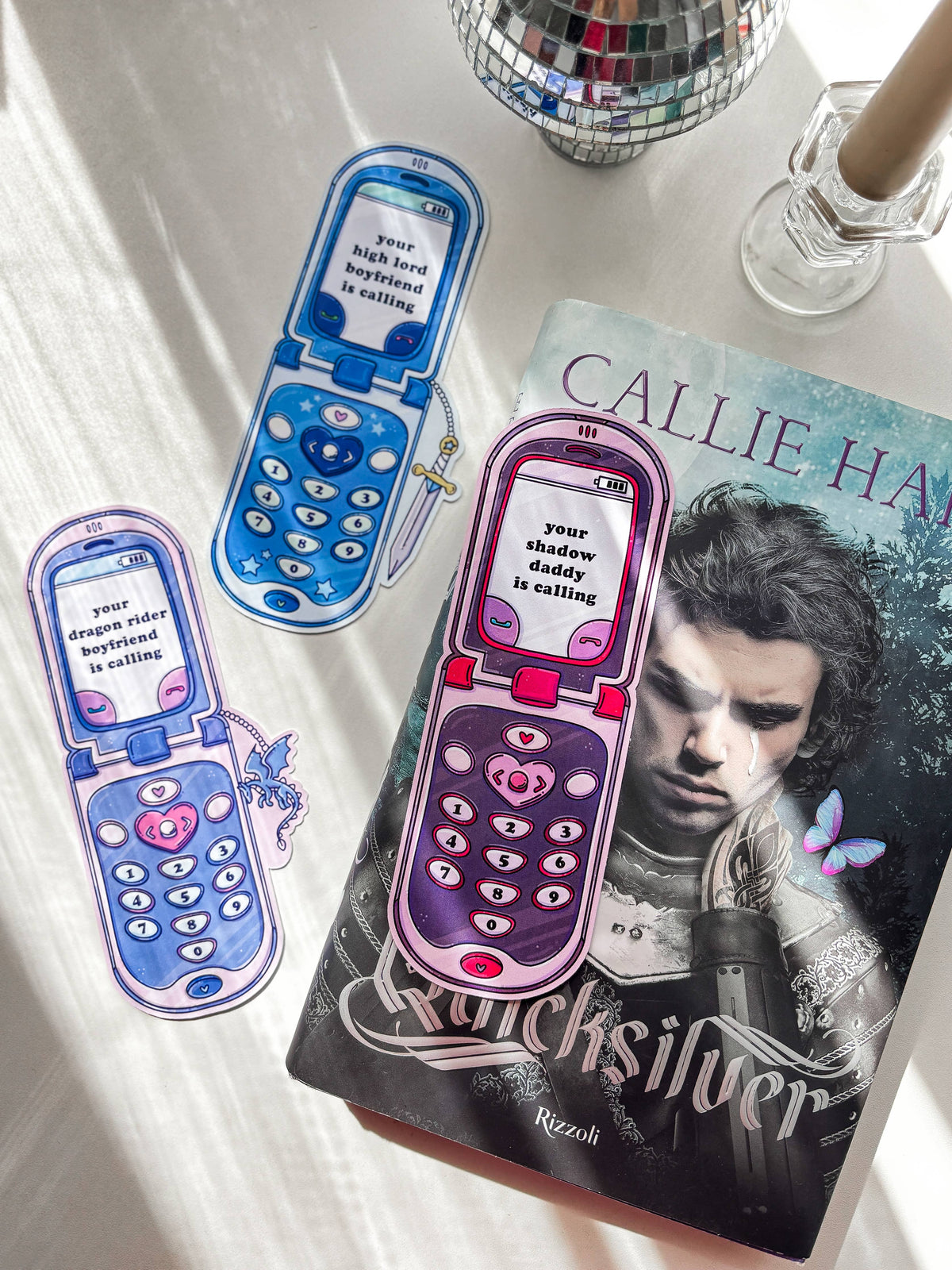 Pink and blue phone-shaped bookmarks on books, with keypad and heart icons.