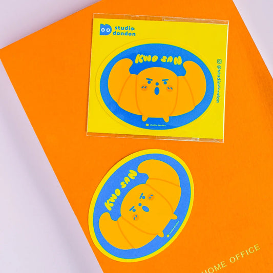 Vinyl croissant sticker, circular blue border with orange character face and dots