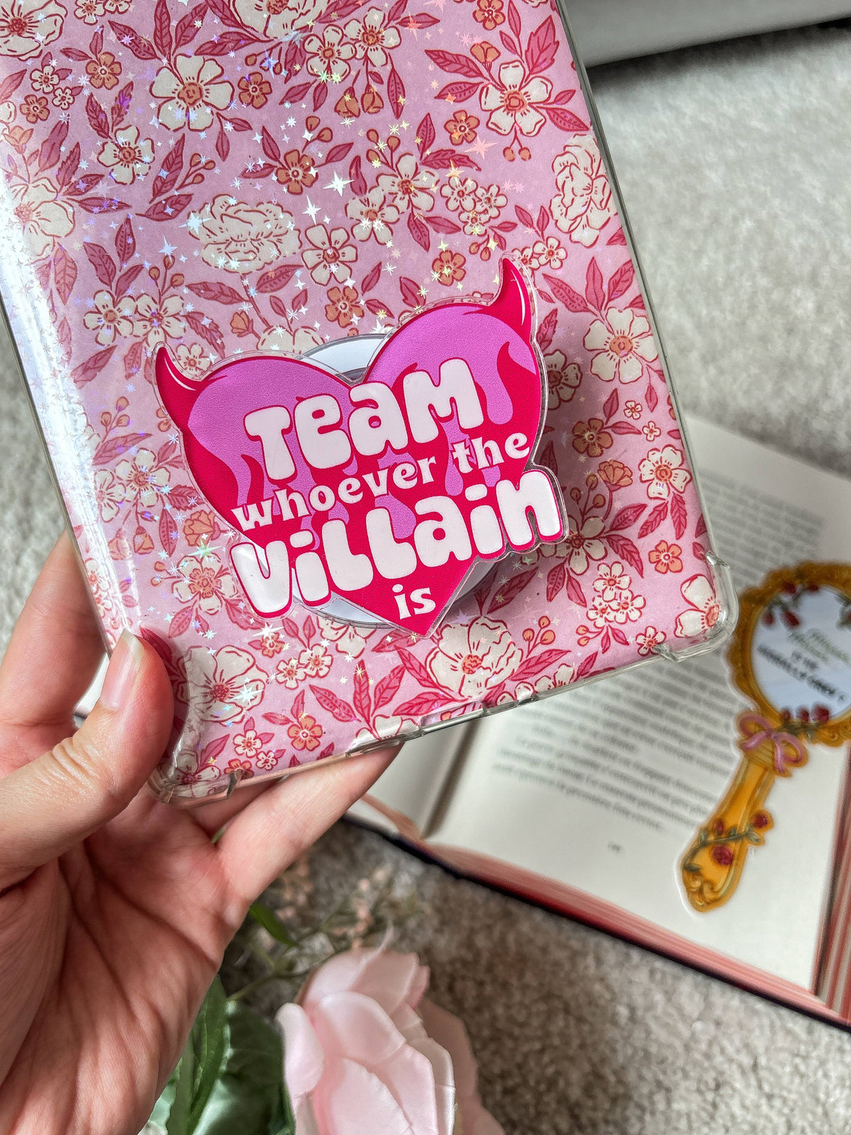 Pink devil heart magnetic grip on floral book cover, 'Team whoever the villain is'