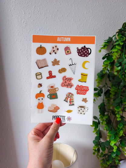 A5 autumn sticker sheet held in hand, with pumpkin, teapot, scarf, and mug stickers