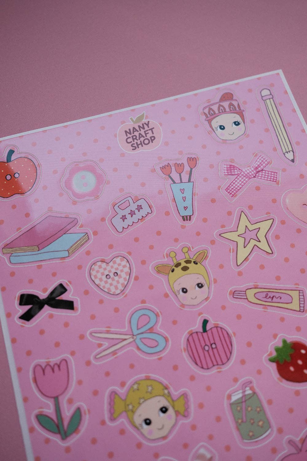 Pink sticker sheet with character faces, stars, hearts, and school stationery shapes