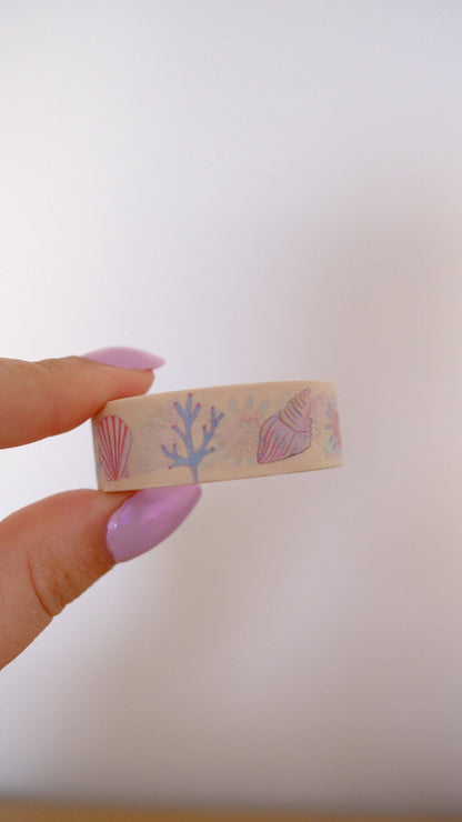 Pastel seashell and coral print washi tape strip held in hand on beige base