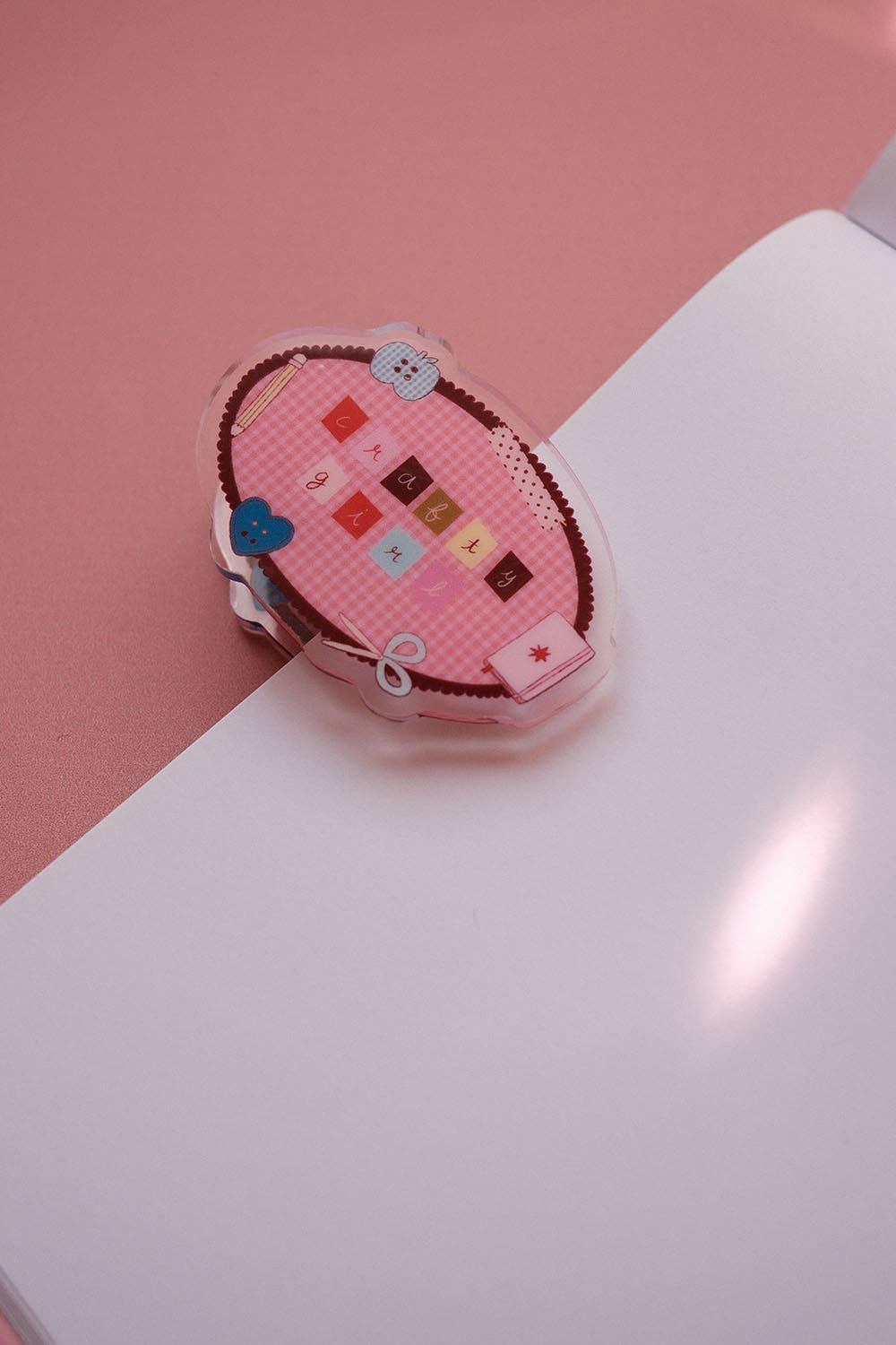 Oval fabric notebook clip with pink design, colorful squares, and small heart charms