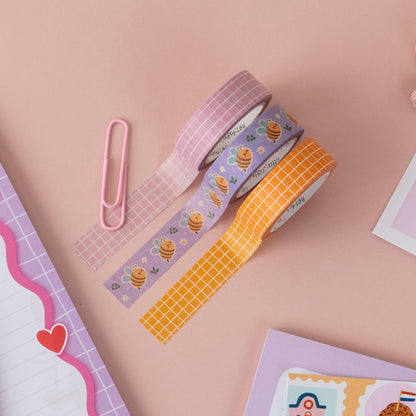 Pink grid washi tape roll among other decorative rolls, crosshatch grid design