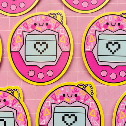 Set of oval virtual pet vinyl stickers on grid paper, pink frames, teal screens with pixel hearts.