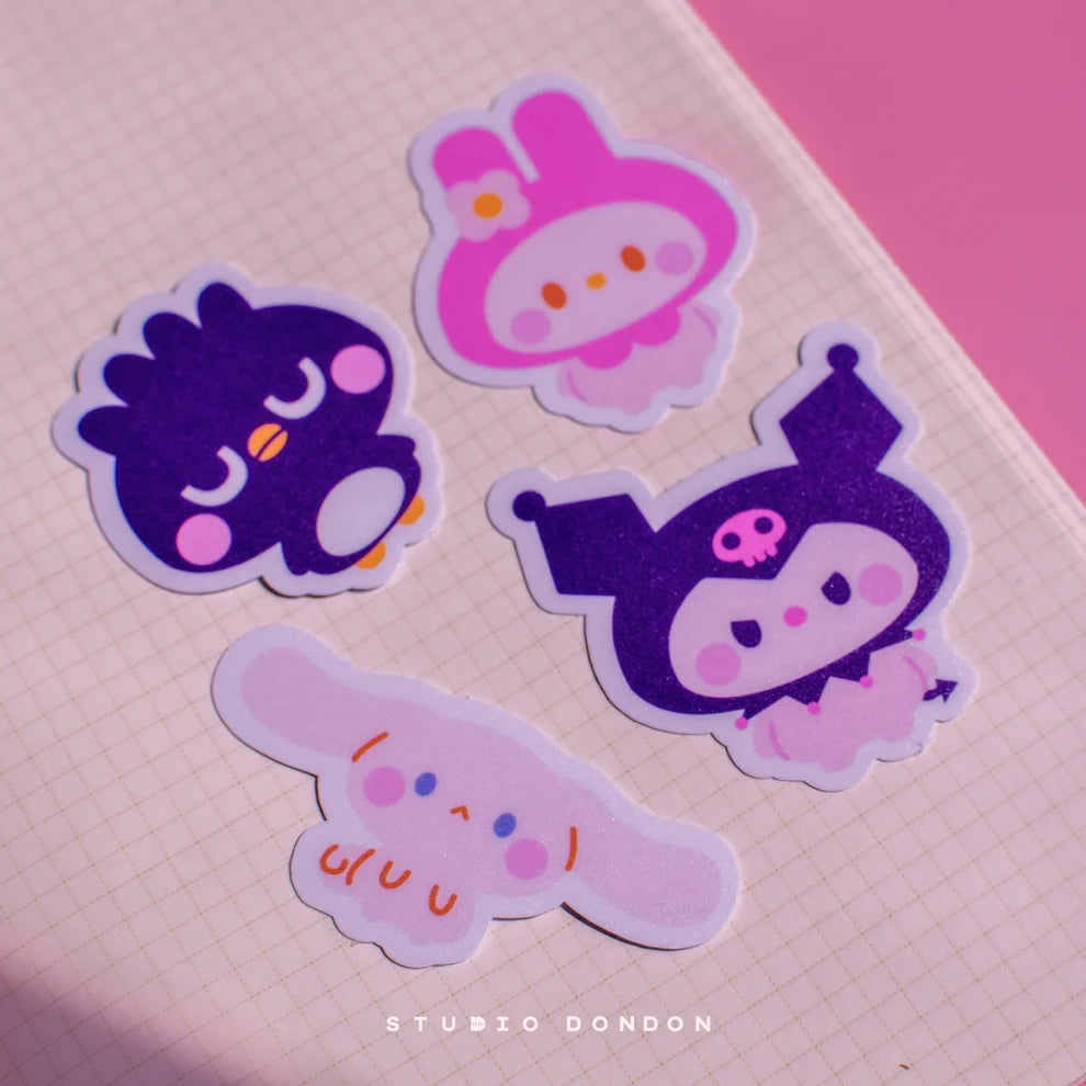 Four vinyl character stickers with purple, pink, and light gray faces, laid on grid paper