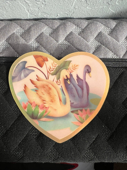 Heart-shaped Swan Friends sticker, 3 inch, showing swans and plants on a black bag
