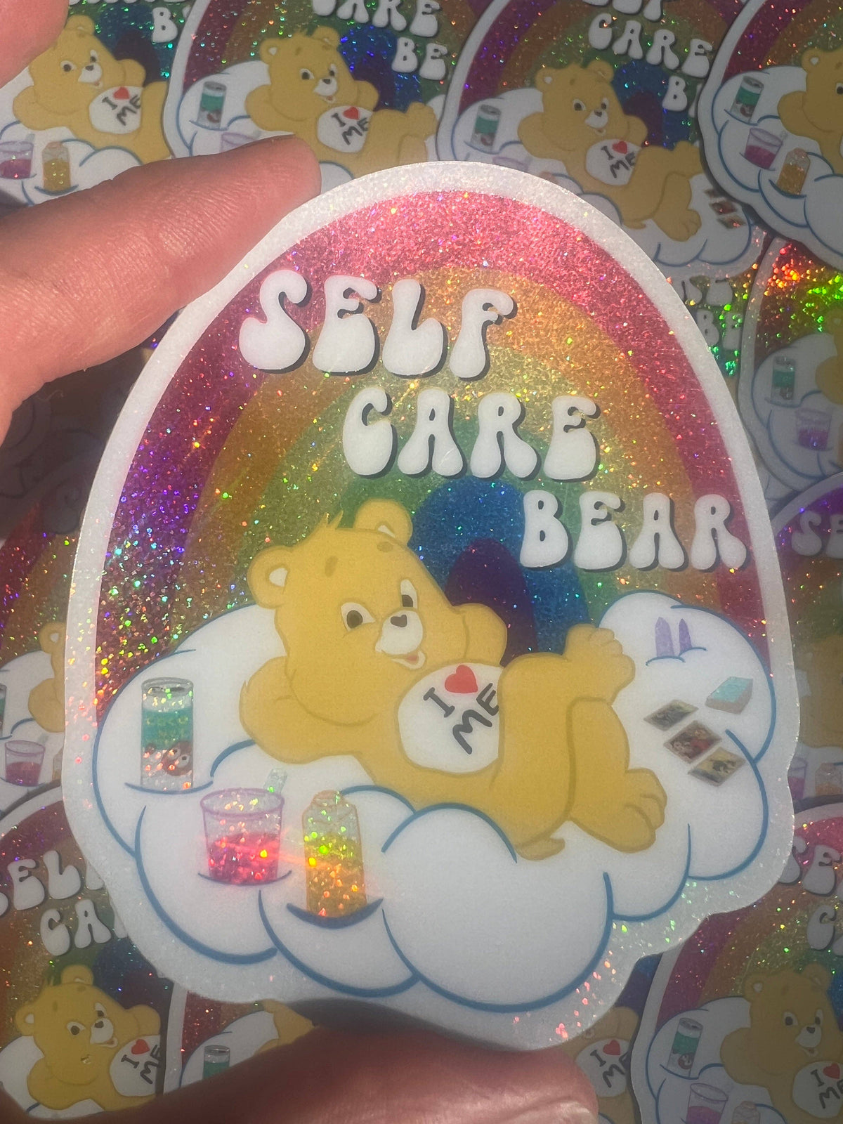 Close-up 3-inch Self Care Bear glitter sticker with bear on cloud and rainbow glitter edge