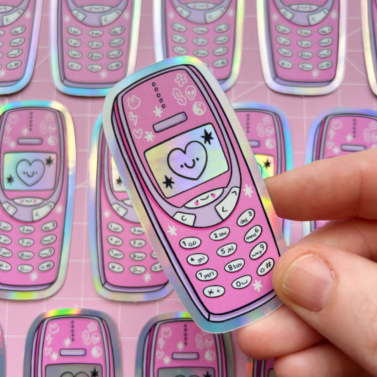 Holographic sticker shaped like a pink phone with hearts and star icons