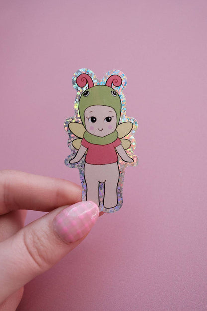 Baby butterfly sticker held by a hand, showing green face, pink shirt, and wings