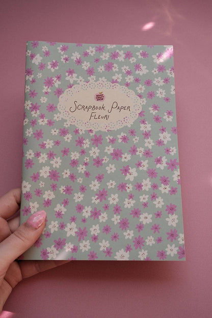 Scrapbook paper sheet with scattered small pink flowers and light gray floral background