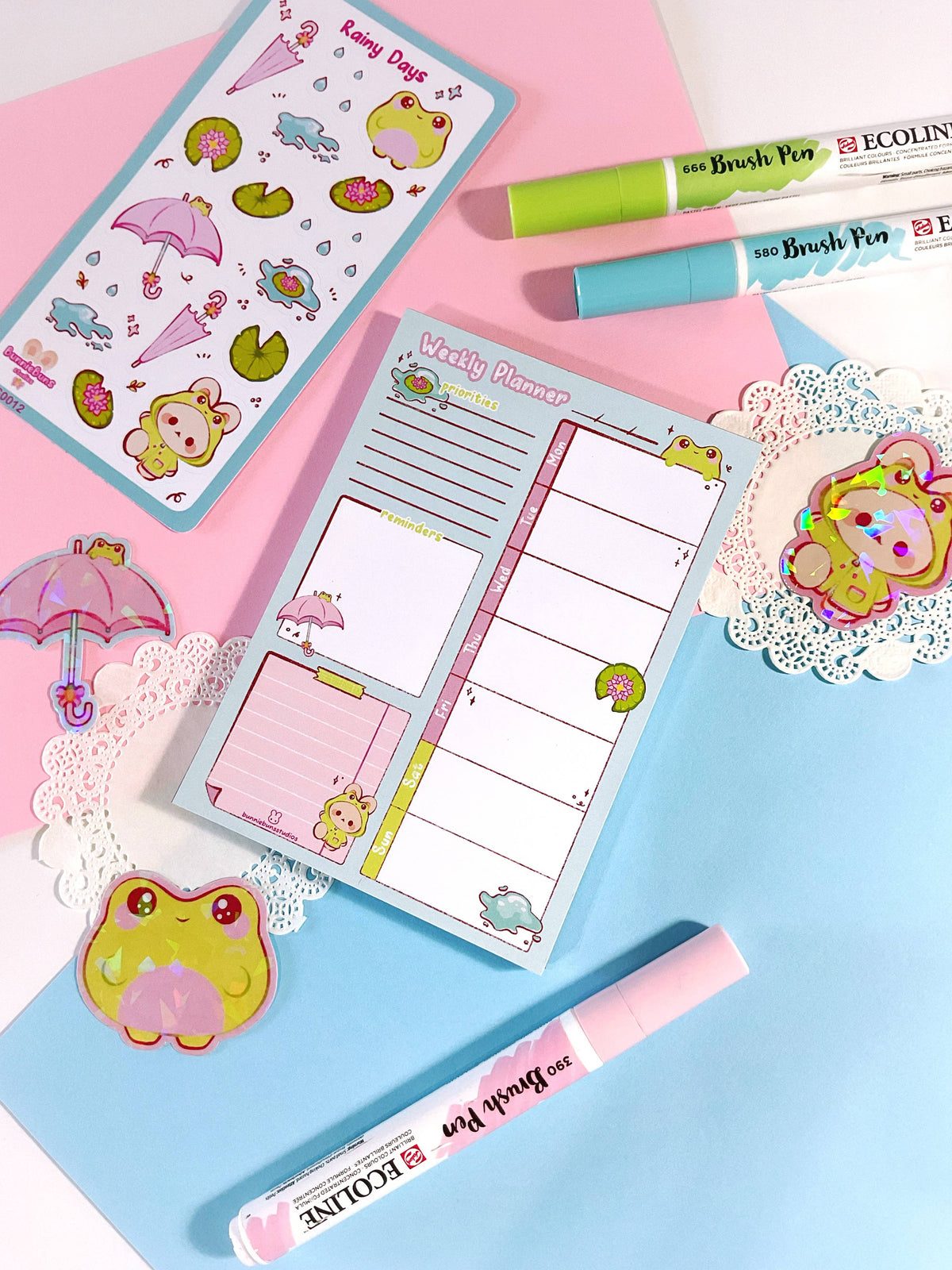 Rainy Days planner open to weekly layout, pink and blue covers with cartoon rain icons