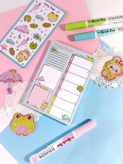 Rainy Days planner open to weekly layout, pink and blue covers with cartoon rain icons