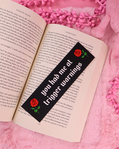 Black romance bookmark with red rose and green text, shown on open book
