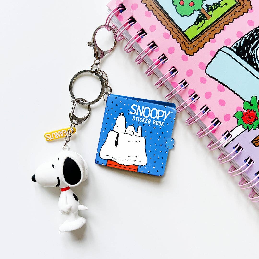 Blue mini sticker book keychain with Snoopy cover and key rings, with other charms nearby