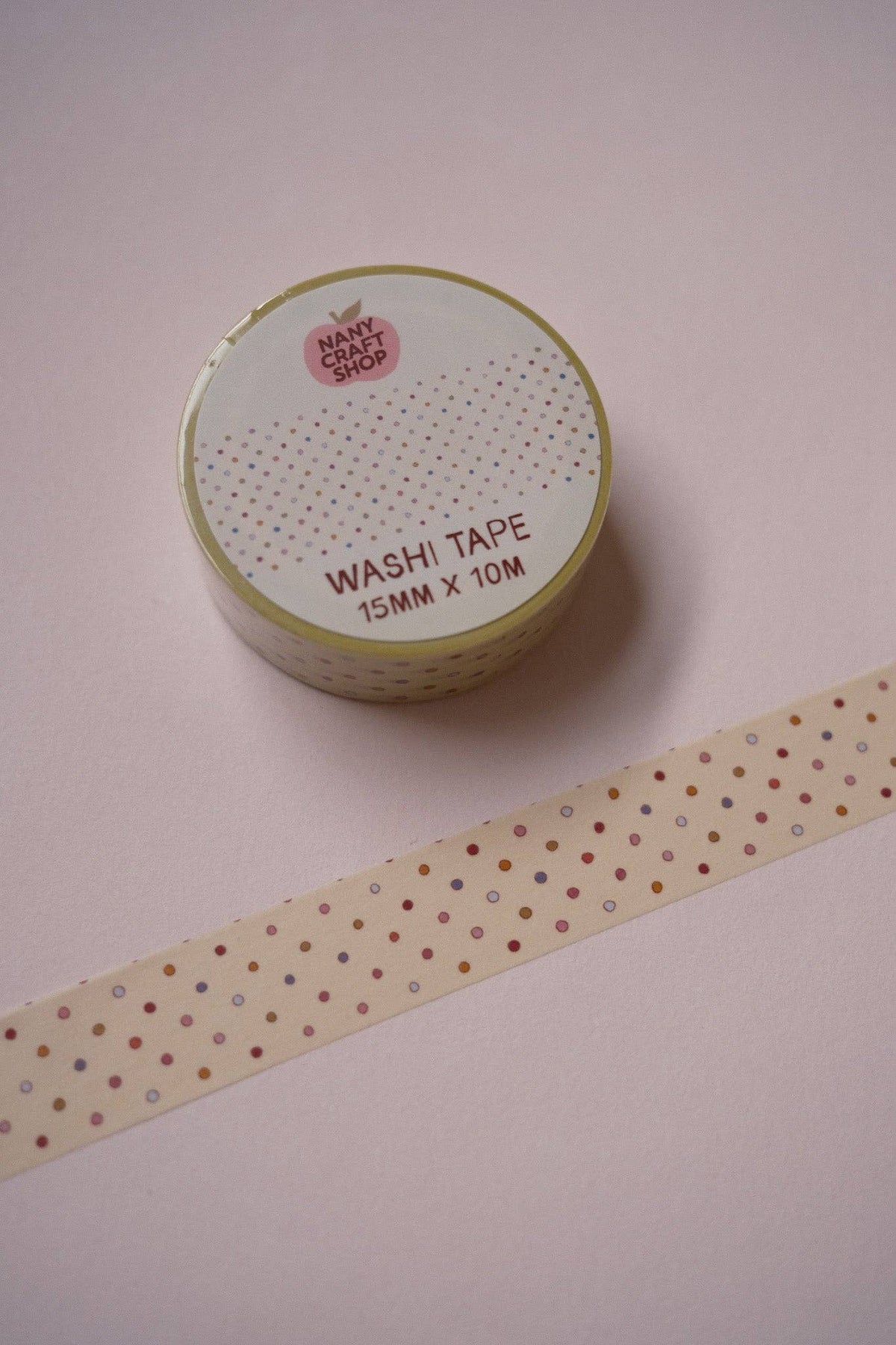 Washi tape roll with beige tape strip featuring multicolor polka dots