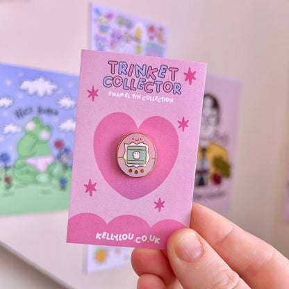 Round mini enamel pin featuring a cartoon virtual pet with a screen and face.