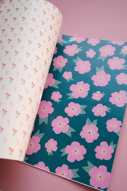 Open scrapbook papers: white small flowers on left, teal sheet with large pink blossoms on right