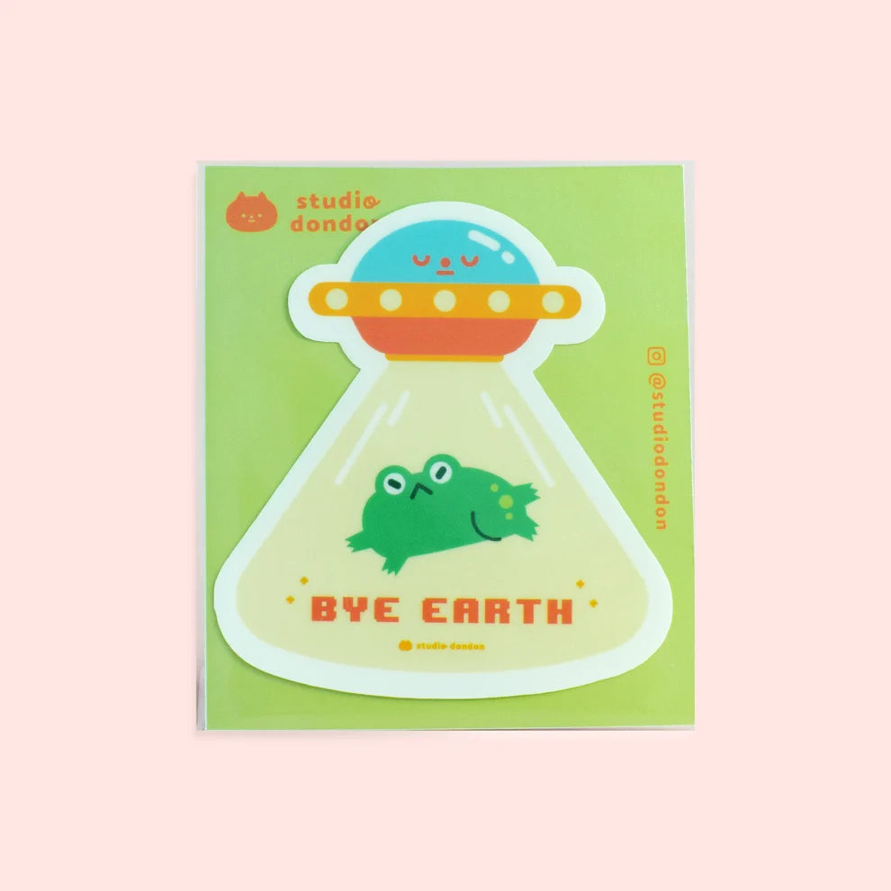 Vinyl sticker of a green smiling frog inside a UFO with 'BYE EARTH' text