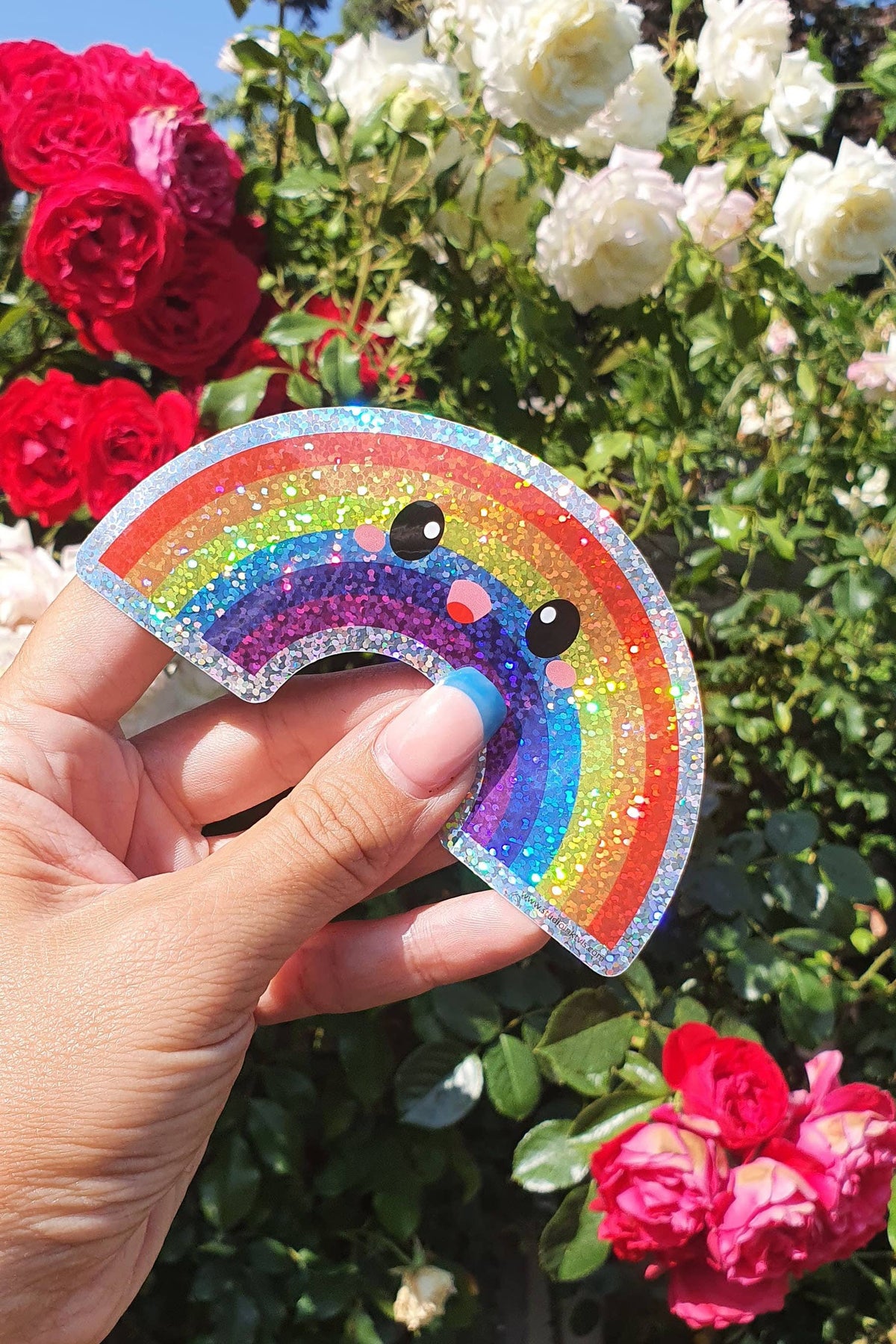 Hand holding rainbow glitter vinyl sticker with bear face; colorful glitter rainbow arc