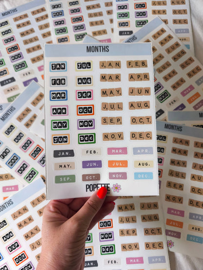 Months A5 sticker sheet in hand, showing grid of colorful month abbreviation stickers