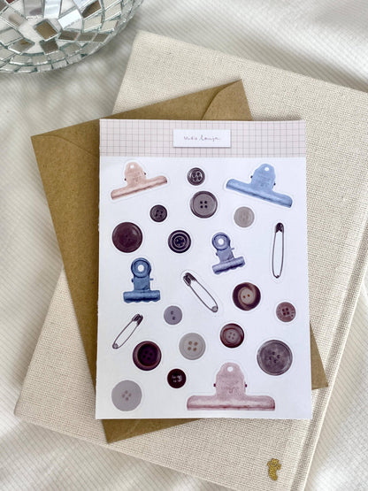 Button-themed sticker sheet with blue and pink clips, round buttons, and needle icons