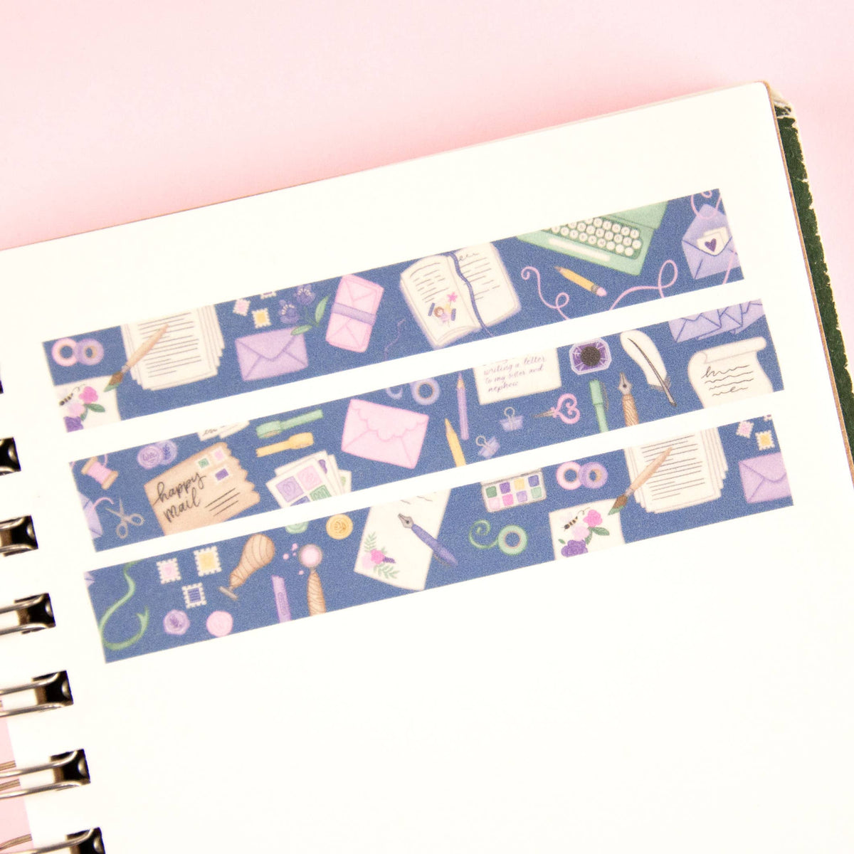 Blue washi tape applied to a notebook edge with stationery icons across the strip.