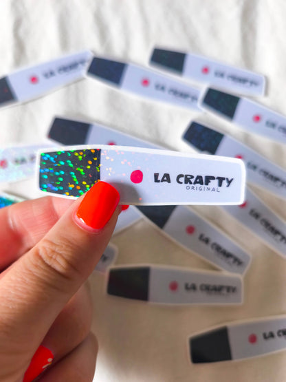 La crafty sticker held by hand, white label with black speckle end and red dot logo