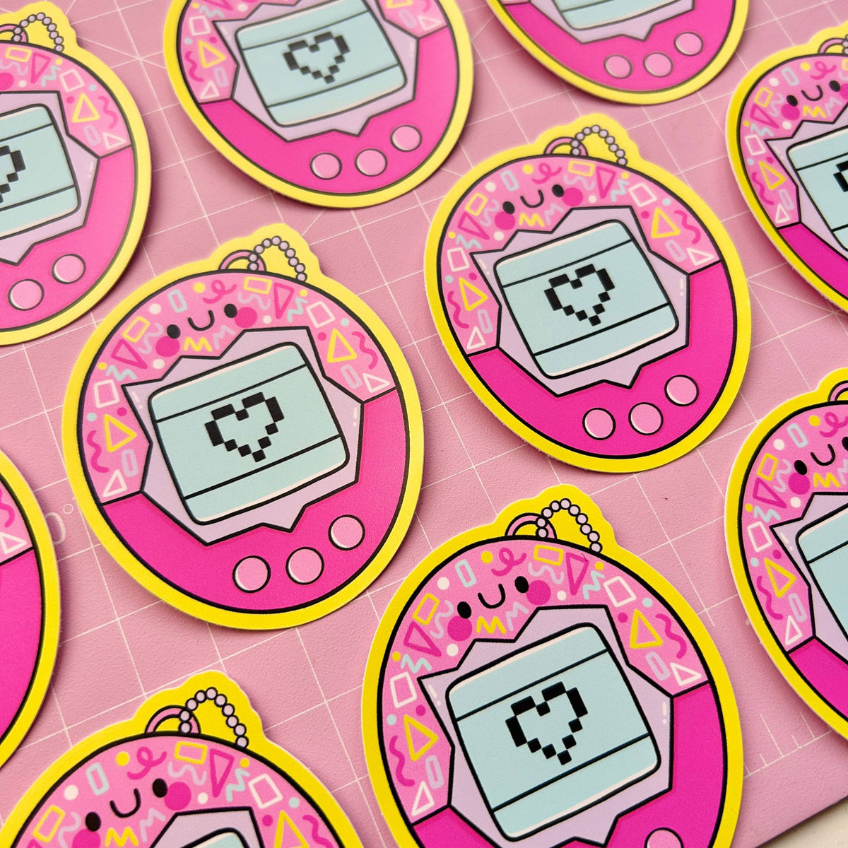 Pink oval virtual pet vinyl sticker with teal screen and pixel heart, outlined in yellow.