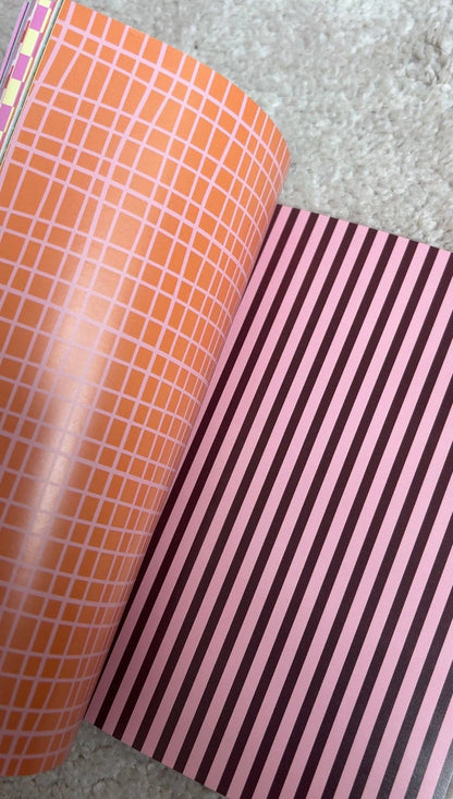 Scrapbook paper spread, orange grid page on left and purple vertical stripe page