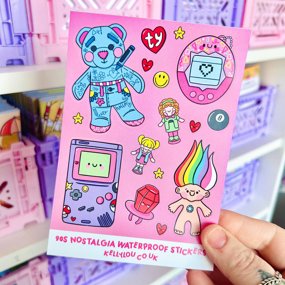 Handheld vinyl sticker sheet with bear, dolls, game console, and heart icons on purple