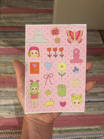 Sticker sheet held in hand, featuring pink baby characters, tulips, hearts, butterfly, gifts