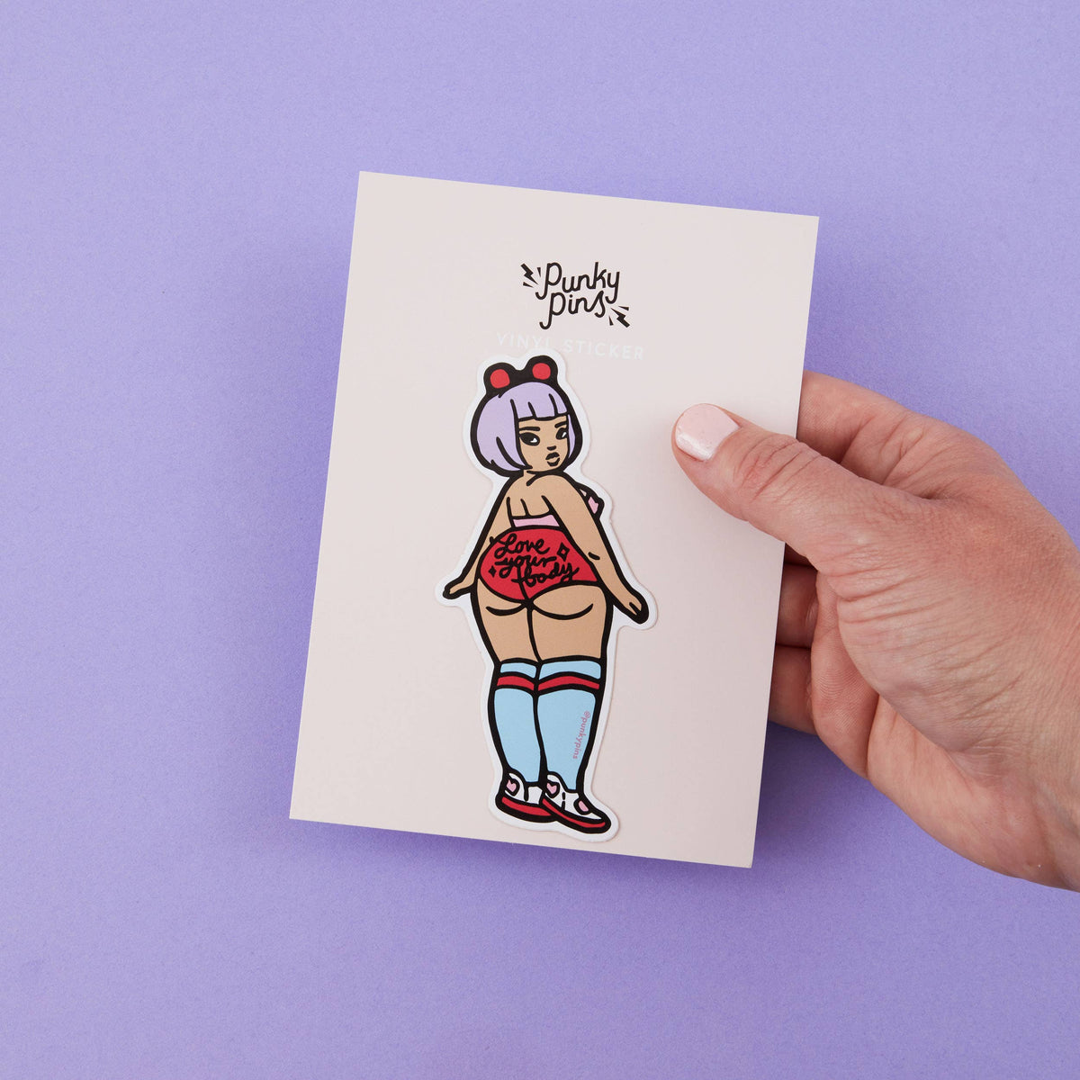 Cartoon vinyl sticker on a card, held by a hand; stylized woman in red top