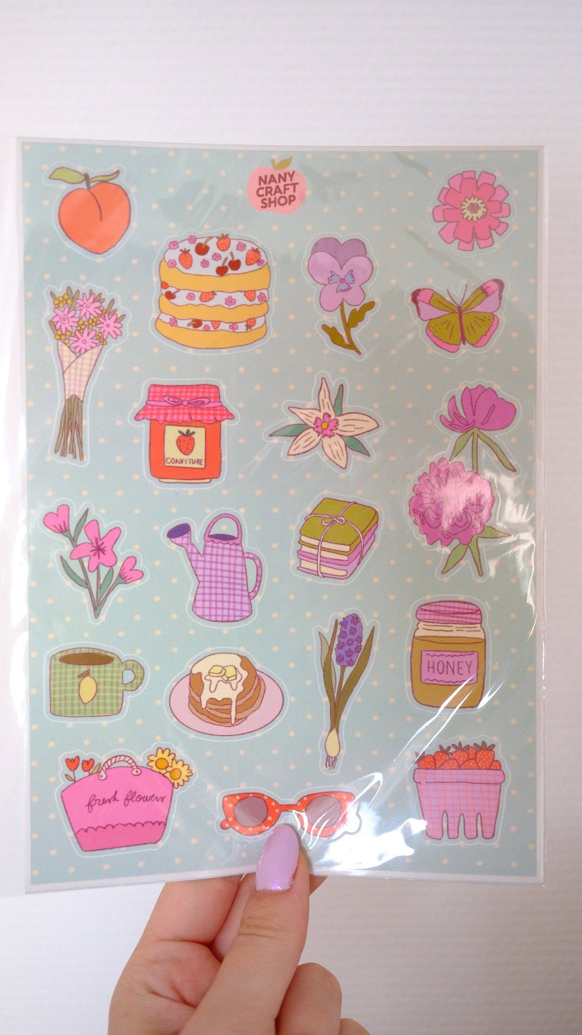 A5 picnic sticker sheet held up, showing pink flowers, cake, honey jar, and butterflies
