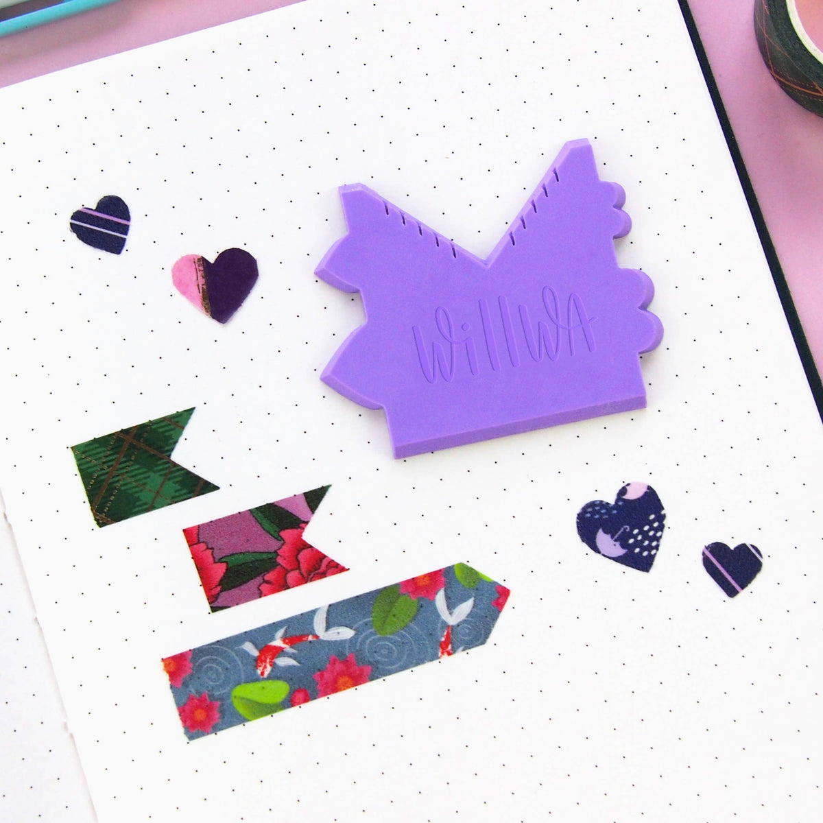 Purple house-shaped washi cutter on a dotted paper surface with small heart shapes