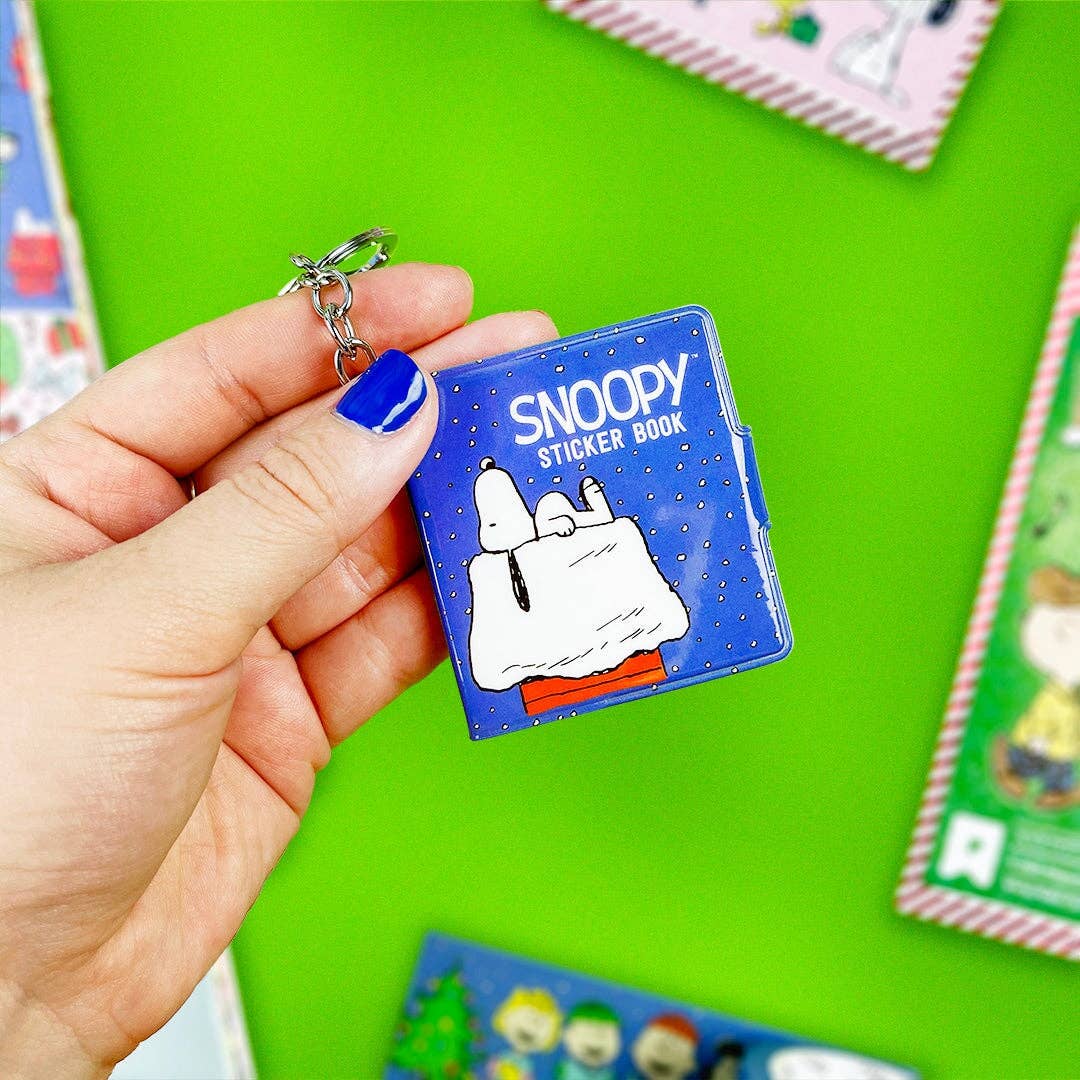 Blue mini sticker book keychain held in hand, Snoopy cover and metal key ring visible