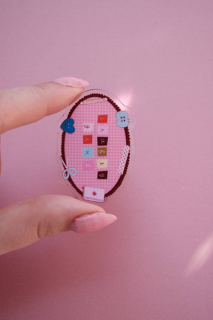 Oval fabric notebook clip held in hands, pink craft design with heart and small button charms