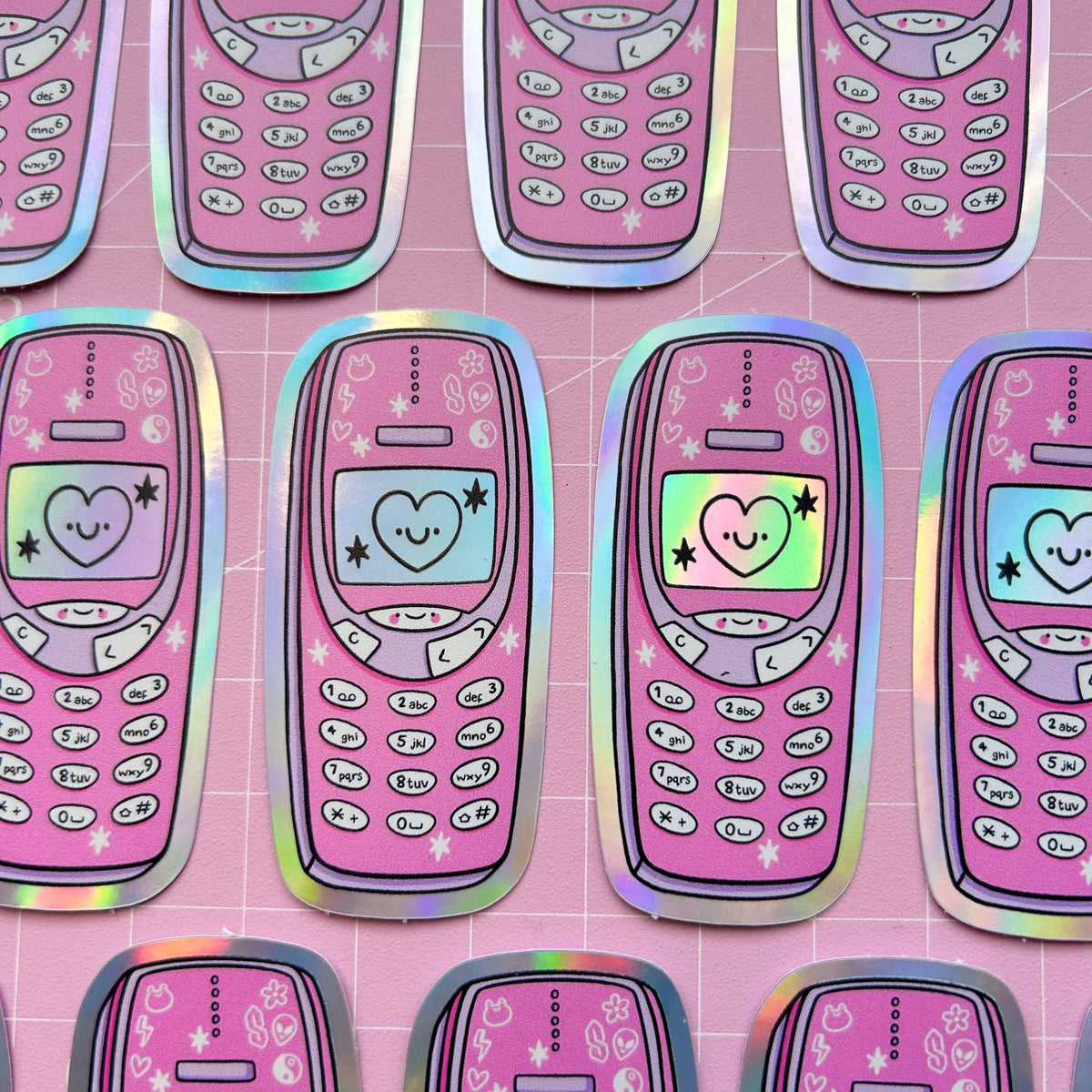 Row of holographic phone-shaped stickers in pink with hearts, stars, and keypad graphics