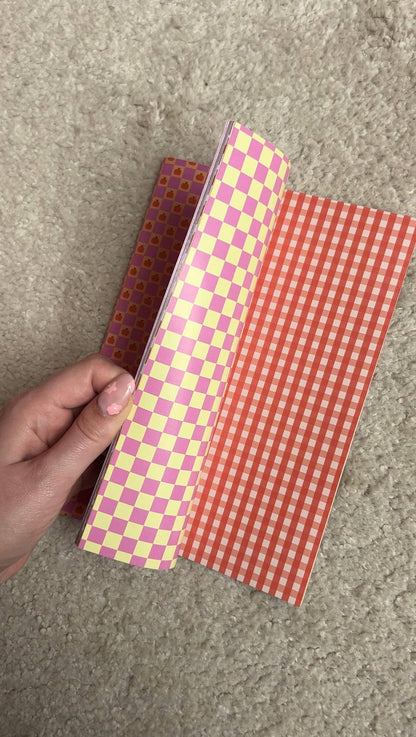 Open scrapbook paper, pink checker pattern on one page and orange grid on the other
