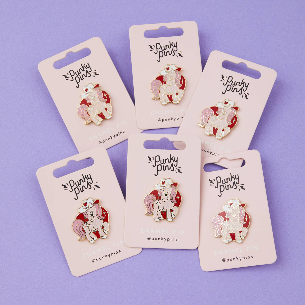 Cowgirl pony enamel pins on backing cards, showing white unicorn with red cowboy hat hearts