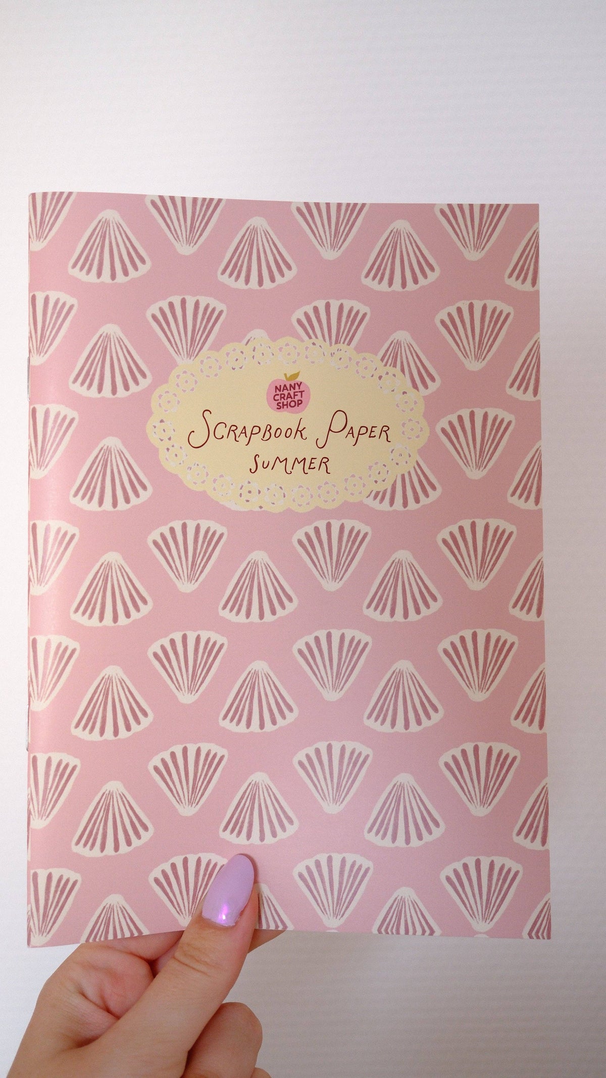 Scrapbook paper sheet held in hand, seashell fan pattern on pink background