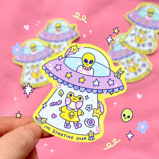 UFO sticker with purple dome, yellow alien, hearts and stars, “Starting over” text
